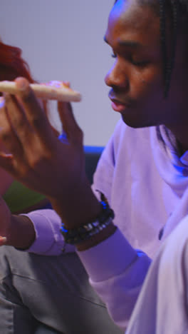 Vertical-Video-Of-Group-Of-Gen-Z-Friends-Sitting-On-Sofa-Eating-Home-Delivery-Takeaway-Pizza-And-Using-Mobile-Phones-1